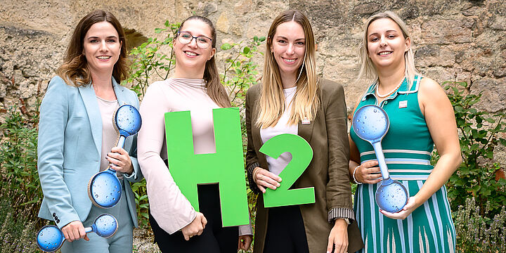 Vier fröhliche Damen halten den Schriftzug "H2" in den Händen