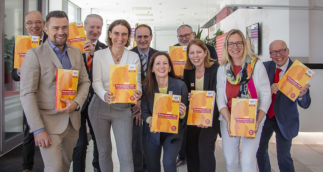 Gruppenfoto im Empfangsbereich. Alle halten das Kursprogramm 2027 hoch.