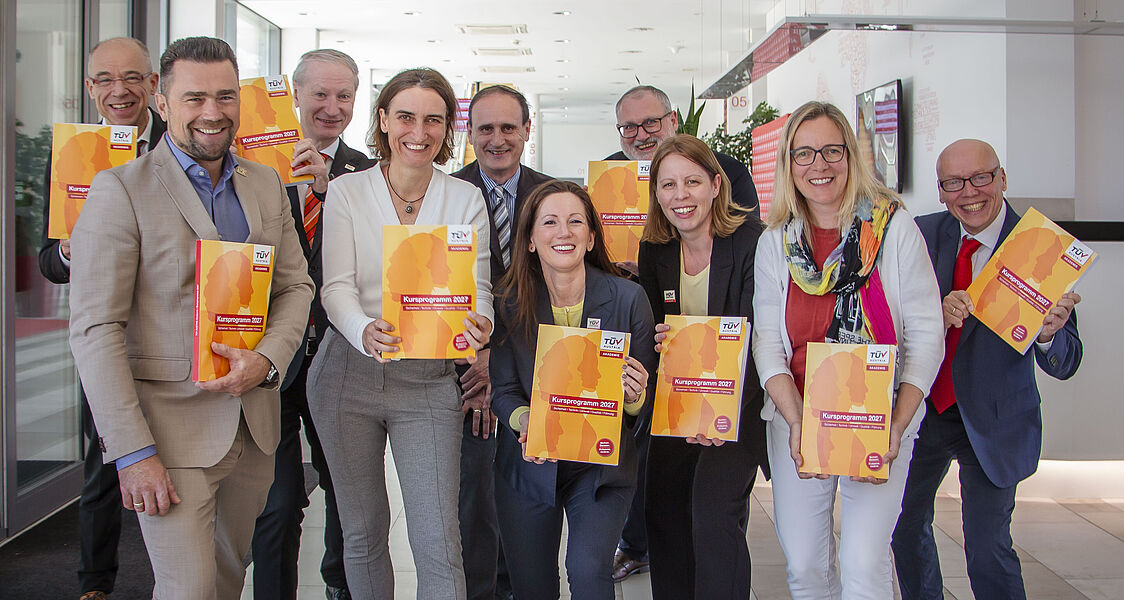 Gruppenfoto im Empfangsbereich. Alle halten das Kursprogramm 2027 hoch.