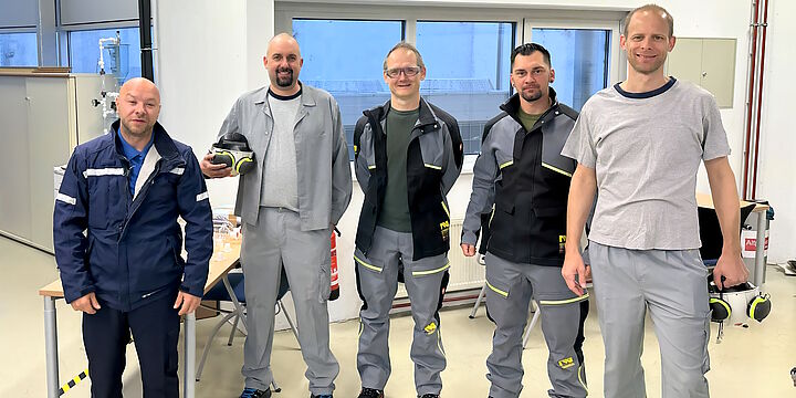 Fünf freundlich lächelnde Herren in Arbeitskleidung.