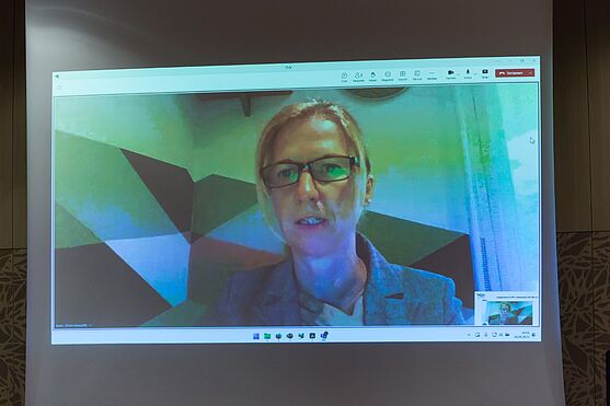 Eine Frau ist per Videocall auf der Leinwand des Vortragssaals zu sehen. Live-online sprach die Referentin Karin Lenhard über ESG-Projekte in der ERSTE Bank.